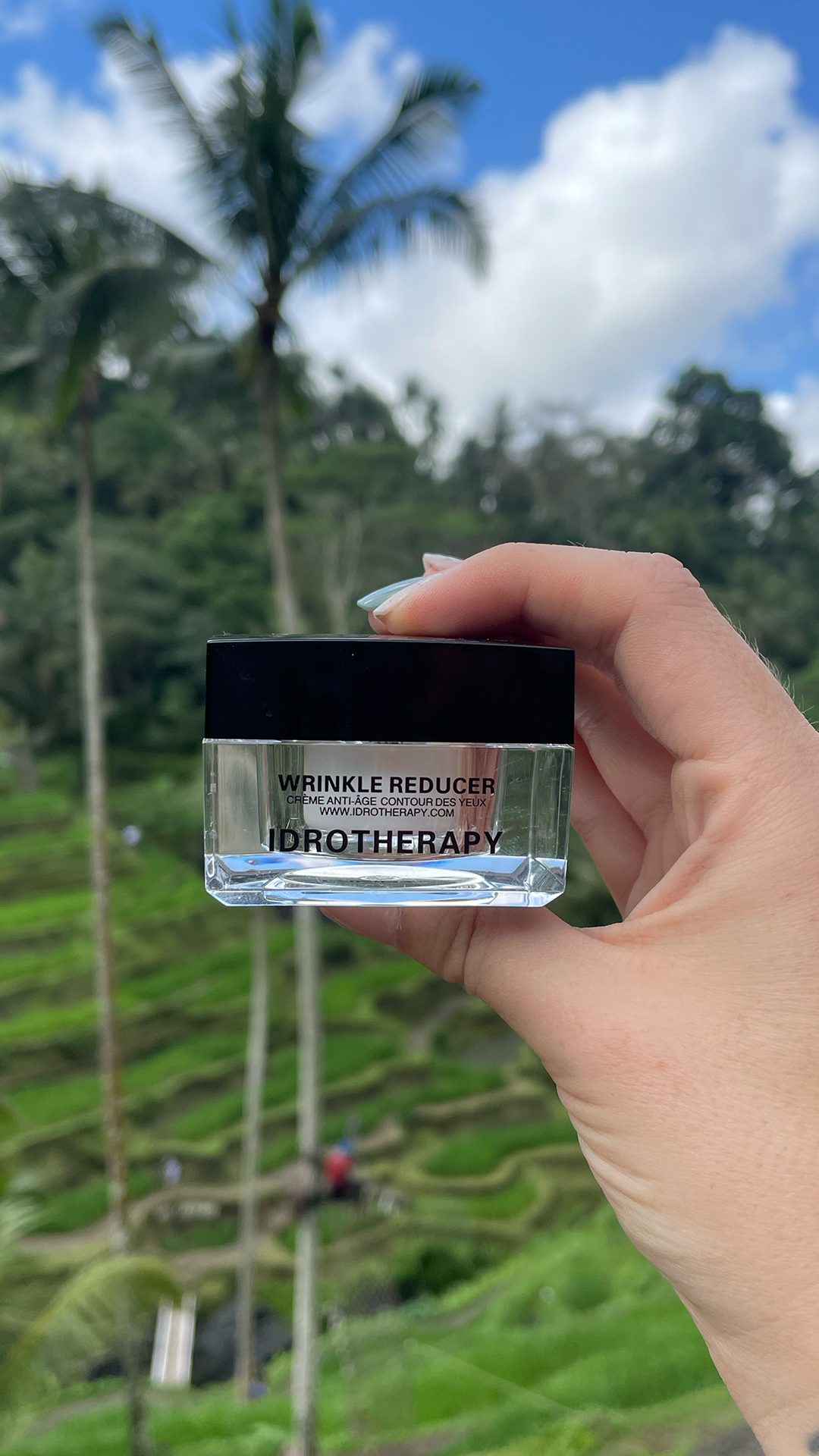 Hand holding a jar of Idrotherapy Wrinkle Reducer against green hills